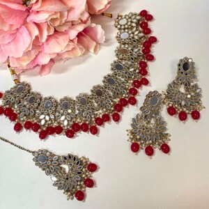Può includere: Un set di collane da sposa indiane rosse e dorate con lavorazione a specchio e accenti di perle. Il set include una collana choker, orecchini e un maang tikka.