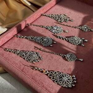 Può includere: Sei pezzi per capelli da sposa in argento e cristallo con catene pendenti e disegni intricati. I pezzi sono disposti su una superficie di velluto rosa.