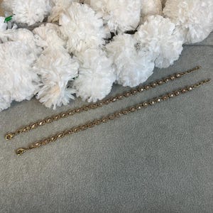 May include: Two matching gold-toned metal chains featuring a series of small, round, light brown faceted crystals set in individual bezels. Each chain is finished with a small lobster claw clasp at one end and a short extender chain at the other.