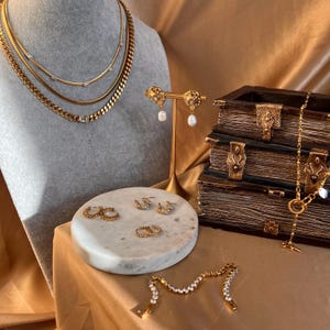 May include: A collection of gold jewellery featuring necklaces, earrings, bracelets and rings. The jewellery is displayed on a marble surface and a wooden box.