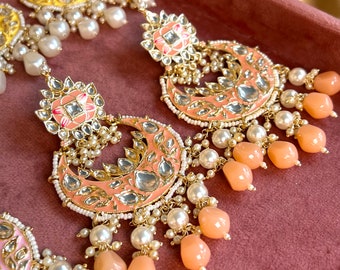 May include: A pair of peach-colored earrings with intricate gold detailing and pearl and peach-colored bead accents.