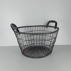May include: A large, oval-shaped wire basket with two black metal handles. The basket is made of thin wire and has a slightly rusted finish.