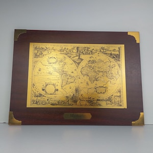 May include: A framed world map with gold foil accents. The map is surrounded by a dark wood frame with gold corner accents. The text "Weltkarte" is visible at the bottom of the frame.