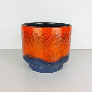 May include: Orange and blue ceramic planter with a textured glaze. The planter has a wide, round opening and a slightly flared base.