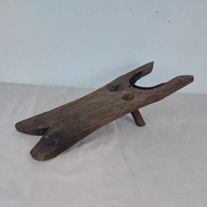 May include: A wooden boot jack with a simple design. The jack is made of dark brown wood and has a single leg.