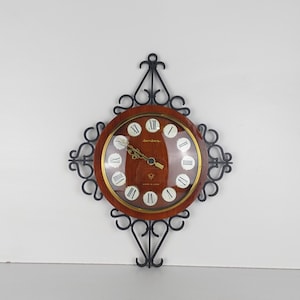 May include: A vintage wall clock with a black metal frame and a round wooden face. The clock face has Roman numerals and the word "Sanitas" printed on it. The clock is made in Japan.