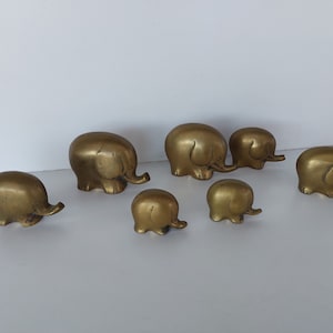 May include: A set of seven gold-colored metal elephant figurines of varying sizes. The elephants are arranged in a line, with the largest elephant at the back and the smallest elephant at the front.