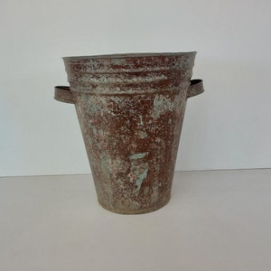 Peut inclure: Un seau en métal vintage avec deux poignées. Le seau est de couleur brun rouille avec de la peinture verte délavée.