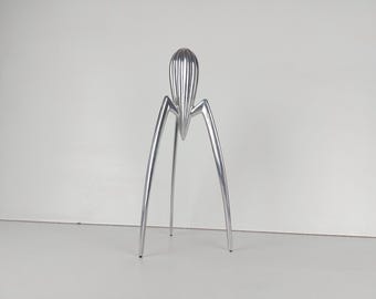 May include: A silver,  aluminum citrus juicer with a unique,  spidery design. The juicer has a tall,  pointed top and four long,  thin legs.