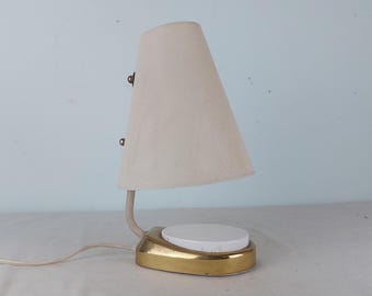 May include: A gold-toned table lamp with a white fabric shade. The lamp has a round base with a white marble top.