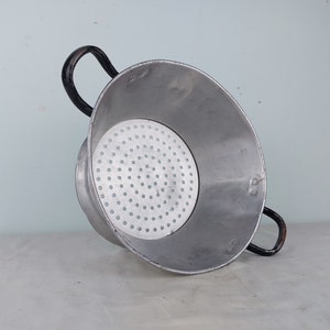 May include: A silver aluminum colander with black handles. The colander has a round bottom and a perforated surface.