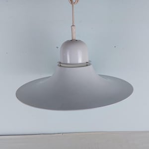May include: A white, mid-century modern pendant light. The light has a wide, shallow, saucer-shaped shade and a cylindrical top. The fixture is suspended from a white cord. The light is a soft, neutral colour.