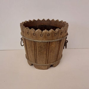 May include: A wooden planter with a decorative top and metal handles. The planter is made of natural wood and has a rustic look.
