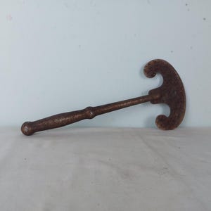 Op de afbeelding: Een roestig metalen gereedschap met een lange steel en een drietandkop. Het gereedschap wordt gebruikt om harde oppervlakken te breken.