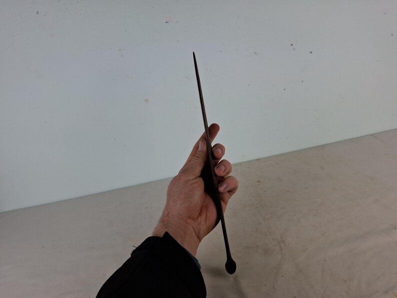 May include: A long, thin, black metal rod with a rounded tip. The rod is held in a person's hand.