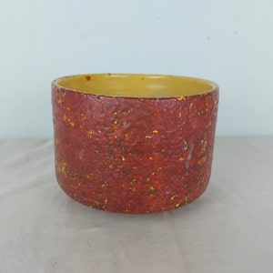 May include: A red and yellow ceramic planter with a textured surface. The planter is round and has a wide opening.