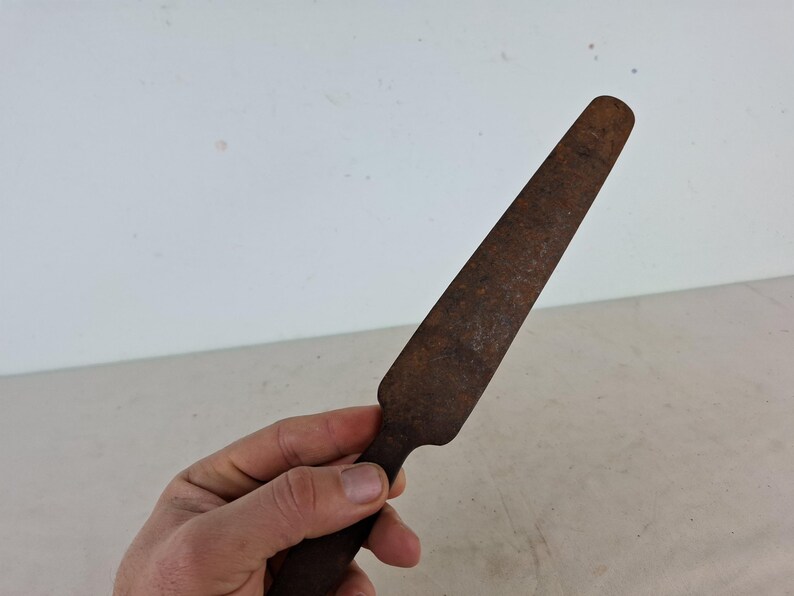 May include: A rusty metal knife with a long, thin blade and a rounded handle.