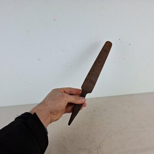 May include: A rusty metal tool with a flat, pointed blade. The tool is about 12 inches long and has a slightly curved handle.