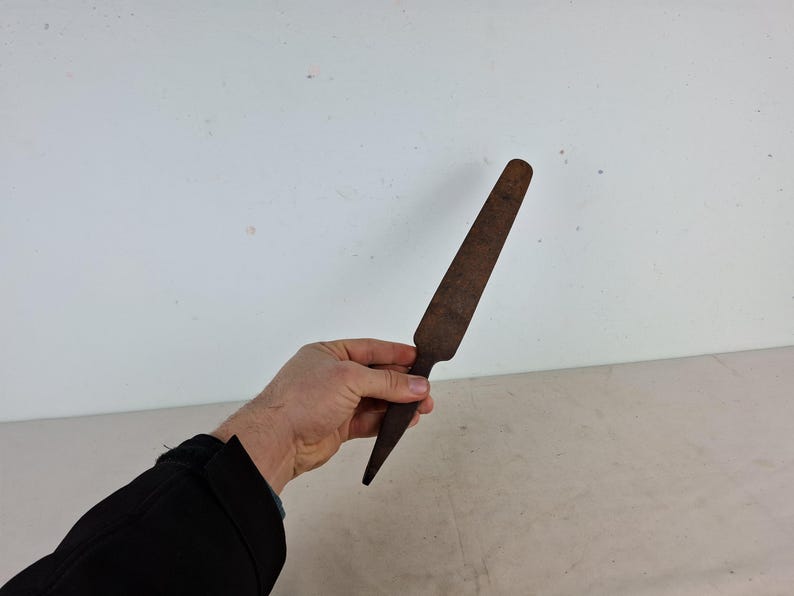 May include: A rusty metal tool with a flat, pointed blade. The tool is about 12 inches long and has a slightly curved handle.