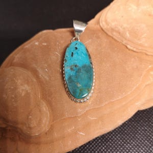 Peut inclure: Pendentif ovale en turquoise avec bélière en argent. La pierre turquoise présente une couleur bleu-vert vibrante avec des motifs de matrice foncés. Le pendentif est serti dans une lunette en argent avec un bord perlé.