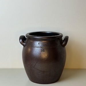 Op de afbeelding: Een bruine keramische pot met twee handvatten. De pot heeft een donker interieur en de tekst "HÖGANÄS" en "5L" zijn zichtbaar op de voorkant. De pot is donkerbruin.