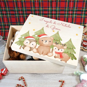 Peut inclure: Une boîte en bois avec un couvercle orné d'un motif de Noël. Le couvercle a un fond blanc avec des arbres verts, un ours brun, un pingouin et un renne. Le texte sur le couvercle est "I regali di Natale di Gioia".