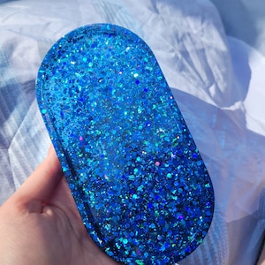 May include: Oval-shaped blue resin tray with a glittery finish. The tray is filled with blue glitter and has a smooth, glossy surface.