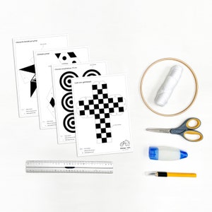 Könnte beinhalten: Ein Bastelset mit gedruckten geometrischen Formen, einem Lineal, einer Schere, Klebstoff, einem Bastelmesser, einer Spule weißen Fadens und einem Stickrahmen. Die bedruckten Blätter zeigen Designs wie Yin-Yang, Kreise und einen Schachwürfel.