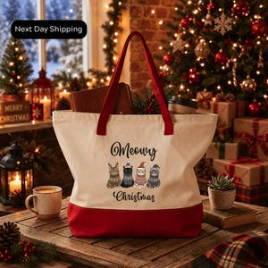 A red and white tote bag with a Christmas-themed design, featuring cats and the text "Merry Christmas" on it, placed on a wooden surface.
