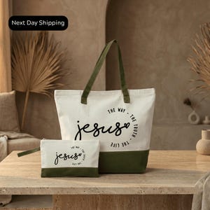 A white tote bag with a green strap and a smaller white bag with a similar design, both featuring the text "The way - The truth - The life - The Jesus" printed on them, placed on a wooden surface.