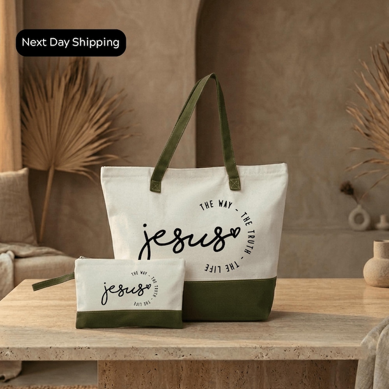 A white tote bag with a green strap and a smaller white bag with a similar design, both featuring the text "The way - The truth - The life - The Jesus" printed on them, placed on a wooden surface.