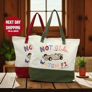 Two colorful tote bags with the text "HOT GIRLS WATCH F1" printed on them, placed on a wooden surface.