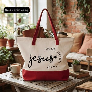 A red and white tote bag with the text "The way - The truth - The life" printed on it, sitting on a wooden table.