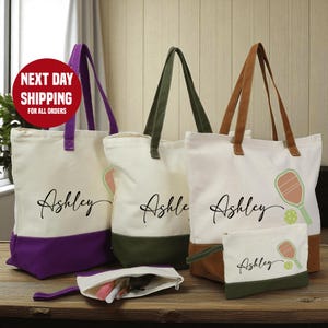 a collection of personalized tote bags and a small bag with the name "Ashley" printed on them, arranged on a wooden surface.