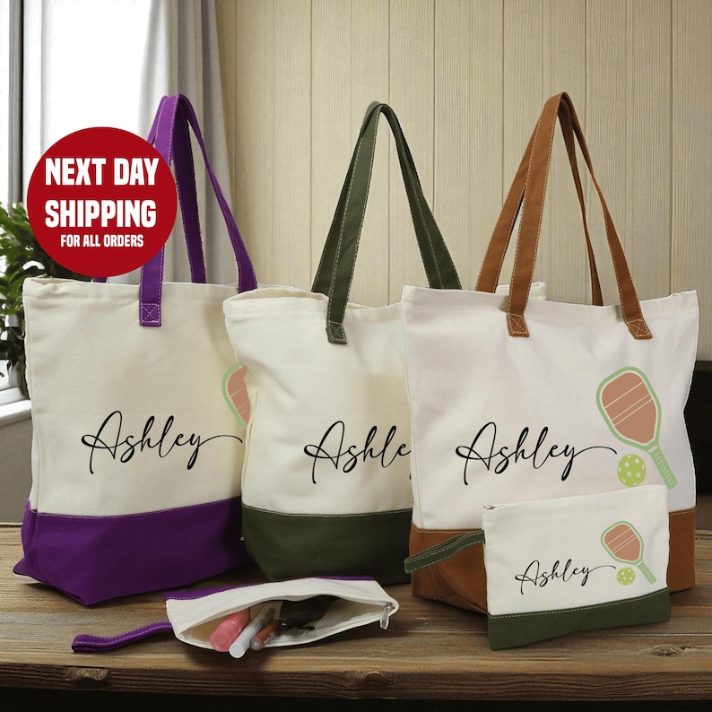 a collection of personalized tote bags and a small bag with the name "Ashley" printed on them, arranged on a wooden surface.