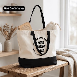 A beige tote bag with black trim and the text "YOUR DESIGN HERE" printed on it, placed on a wooden surface.