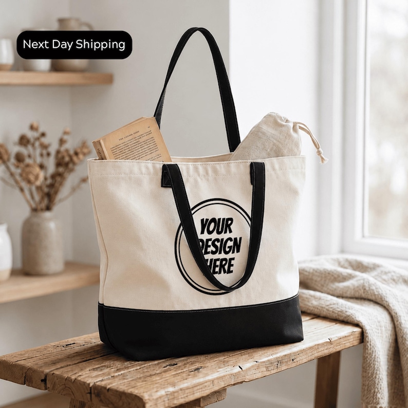 A beige tote bag with black trim and the text "YOUR DESIGN HERE" printed on it, placed on a wooden surface.