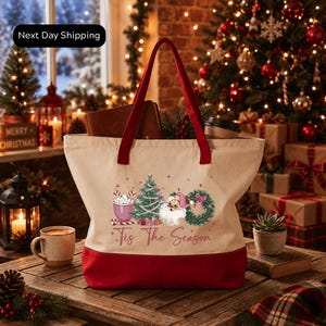 A festive Christmas scene with a red and white tote bag featuring a Christmas tree and other holiday decorations, placed on a wooden table.