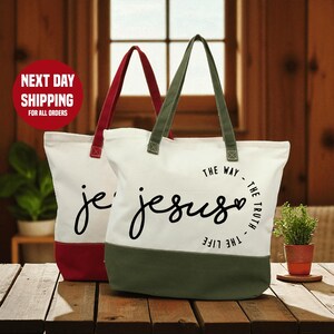 Two tote bags with the text "The way - the truth - the life" printed on them, placed on a wooden surface.