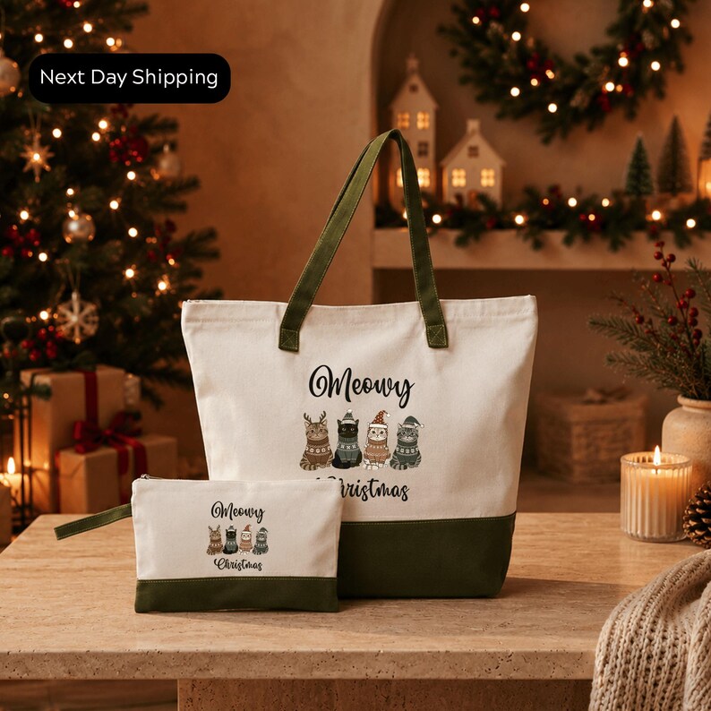 A white tote bag with a green handle and a smaller bag with a similar design are displayed on a wooden surface, with a Christmas tree and holiday decorations in the background.