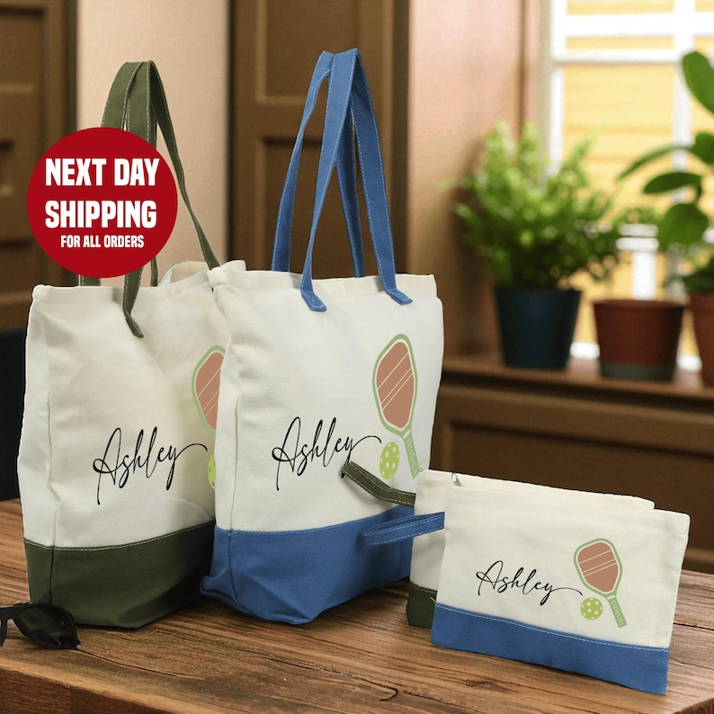 a set of three tote bags with personalized names printed on them, placed on a wooden surface.
