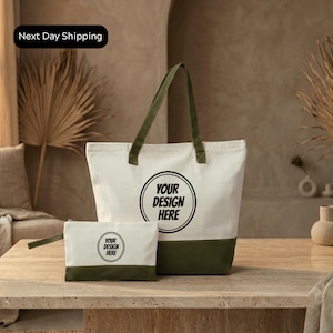 A large white tote bag with a green trim and a smaller white bag with a similar design are displayed on a wooden table.