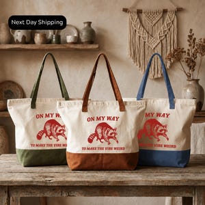 Three tote bags with the same design, featuring a raccoon and the text "ON MY WAY TO MAKE THE VIBE WEIRD".