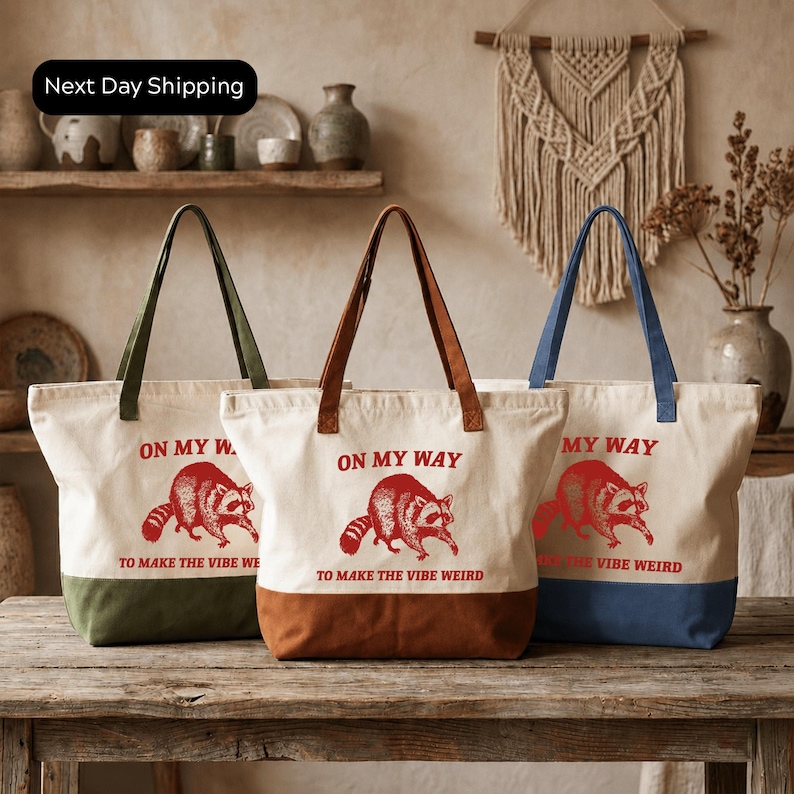 Three tote bags with the same design, featuring a raccoon and the text "ON MY WAY TO MAKE THE VIBE WEIRD".