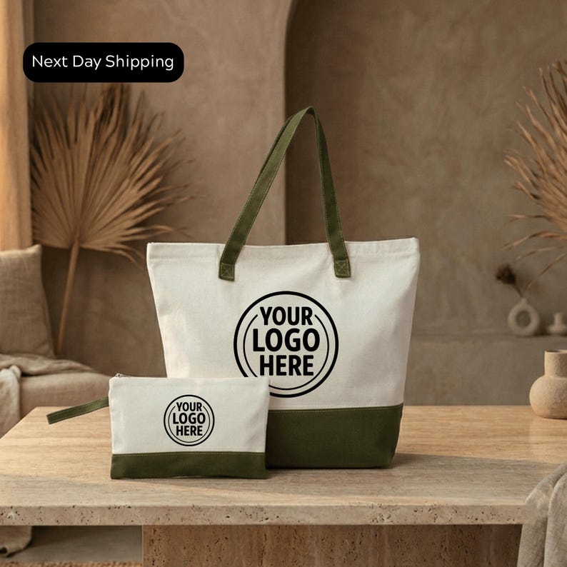 a white tote bag with a green trim and a smaller white bag with a green trim, both placed on a wooden surface.