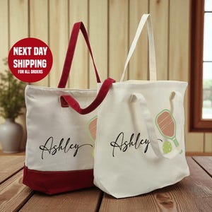 Two tote bags with personalized names printed on them, placed on a wooden surface.