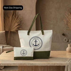 A large white tote bag with a navy blue anchor design and a smaller white bag with a similar navy blue anchor design are displayed on a wooden table.