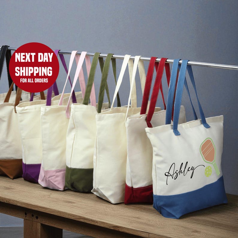 A row of colorful tote bags with personalized names on them, displayed on a wooden shelf.