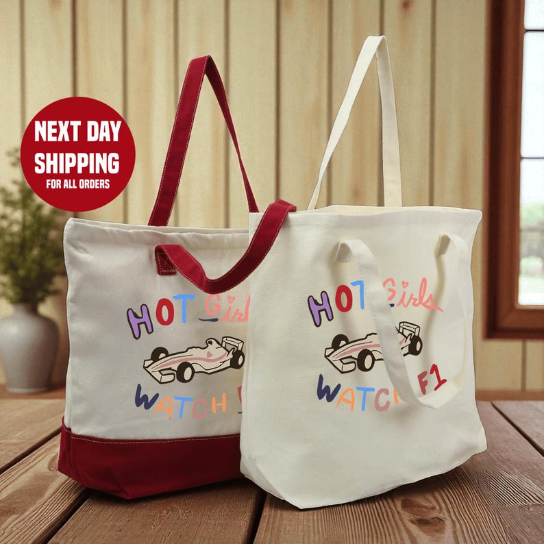 Two tote bags with the text "HOT GIRLS WATCH F1" printed on them, placed on a wooden surface.