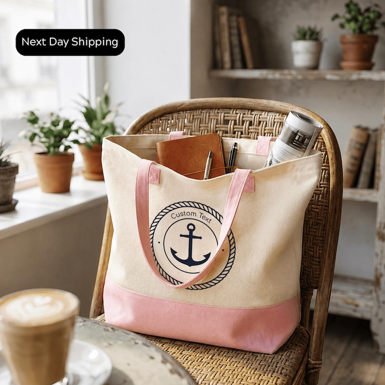 A beige tote bag with a navy blue anchor symbol and the text "Custom Text" is sitting on a wicker chair in a room with potted plants and a window.